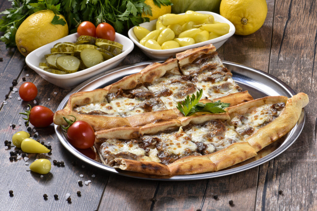 Restoran yemek fotoğrafçısı çekimi: metal servis tabağında kıymalı ve kaşarlı pide, yanında turşu, domates ve limon